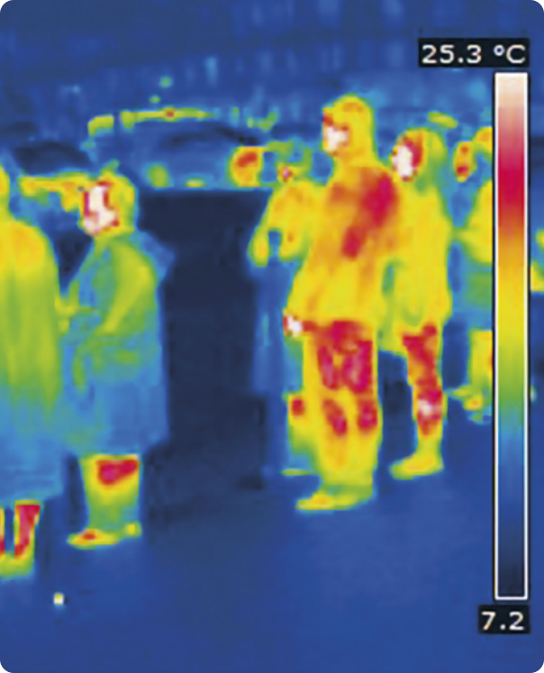 Fotografia de pessoas em infravermelho. A silhueta dos corpos das pessoas possui tons de cores como o amarelo e vermelho, enquanto o ambiente e partes das roupas das pessoas apresentam cores como o verde e azul. Na imagem há uma barra vertical, colorida com a escala em graus Celsius. Na parte inferior da barra, está escrito 7 vírgula 2 graus Celsius. Na parte superior da barra, está escrito 25 vírgula 3 graus Celsius. A barra mostra um gradiente de cores que passa, de baixo para cima, pelo azul escuro, azul claro, verde, amarelo, laranja, vermelho e branco na parte superior.