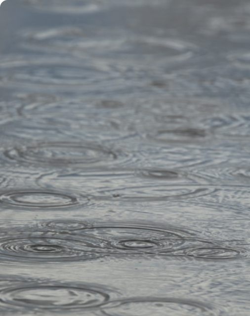 Fotografia da superfície da água, caindo pingos de chuva, formando ondas em formato esférico na superfície.