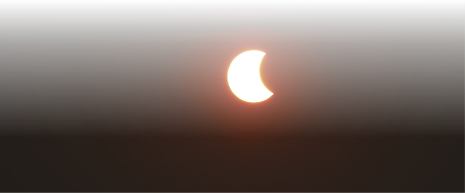 Fotografia de um eclipse parcial do Sol. O círculo iluminado que forma a imagem do sol está encoberto por uma sombra em aproximadamente um terço. O céu está escuro.