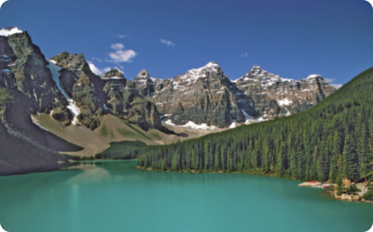 Fotografia de uma paisagem, montanhas com cumes pontiagudos com neve e um lago.