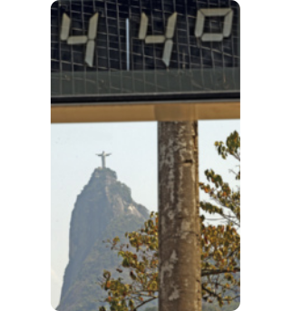 Fotografia de uma parte de um termômetro de rua, marcando quarenta e quatro graus Celsius. Ao fundo, em cima de um morro encontra-se o cristo redentor.