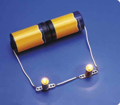 Fotografia de um resistor cilíndrico, na posição horizontal, com um fio saindo de cada lado, ligados á duas lâmpadas acesas, na mesma fila.
