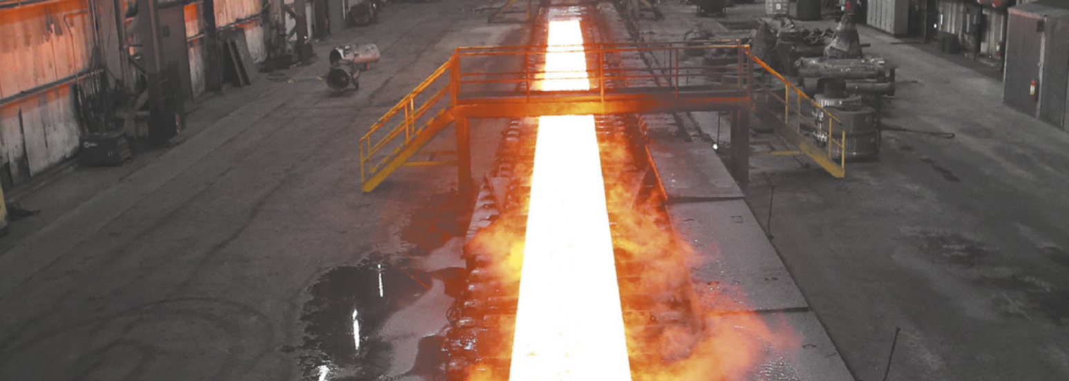 Fotografia de uma siderúrgica. Há uma canaleta cheia de metal derretido, emitindo uma luz alaranjada.