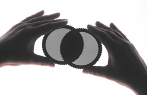 Fotografia das mãos de uma pessoa segurando dois filtros circulares, um sobre o outro, perpendicularmente.