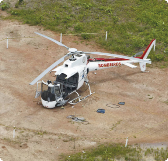Fotografia de um helicóptero no chão com a lataria partida em pedaços.
