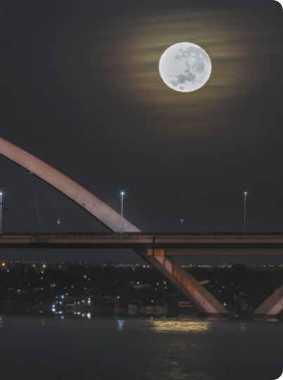 Fotografia da Lua no céu noturno. Abaixo uma ponte.