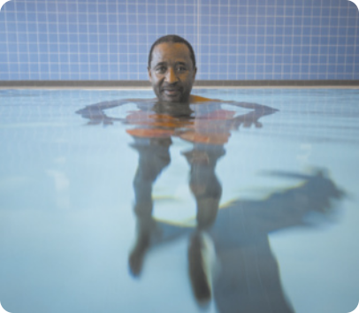 Fotografia de uma pessoa dentro da água em uma piscina. A imagem da pessoa refletida na água fica alterada.