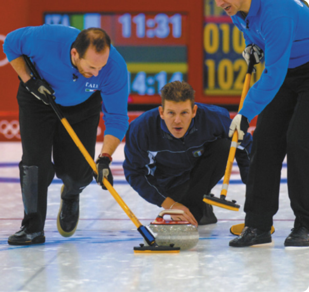 Fotografia de três homens jogando Curling. Na imagem os homens estão em uma quadra, com uma camada de gelo. Eles empurram uma bola com rodos. eles usam roupa de frio.
