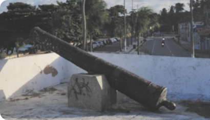 Fotografia de um canhão antigo, apoiado em uma pedra, apontando para cima.