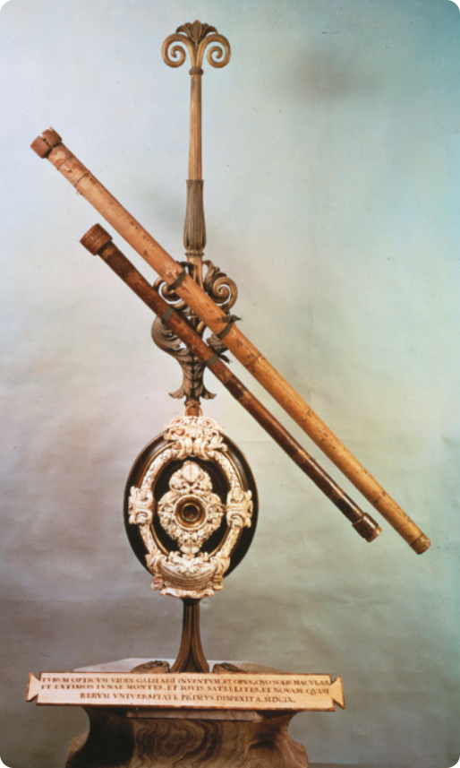 Fotografia dos telescópios usados por Galileu Galilei. Os telescópios são feitos de madeira e estão dispostos em cima de um suporte de metal, decorado com arabescos.