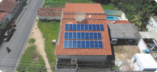 Fotografia de cima de um telhado de uma casa, com painéis solares enfileirados e uma antena circular.