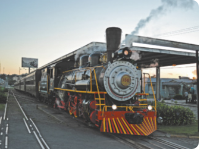 Fotografia de uma locomotiva de trem, soltando vapor, pela chaminé.