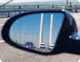 Fotografia de um espelho retrovisor de um carro. No espelho a imagem de carros refletida.