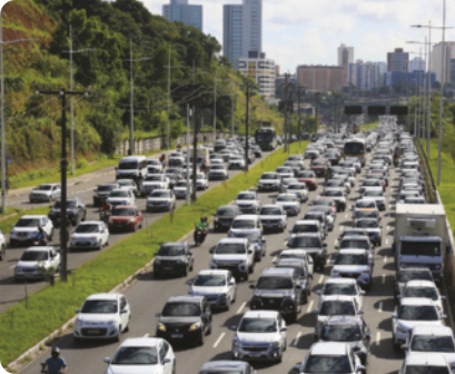 Fotografia de um intenso congestionamento de automóveis em duas grandes avenidas. Ao fundo, vemos edifícios da cidade.