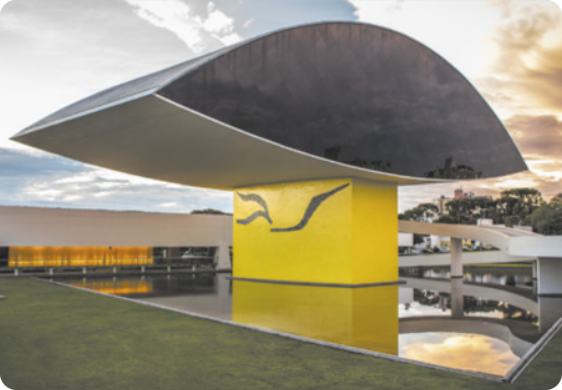 Fotografia da edificação do Museu Oscar Niemeyer. O prédio é composto por uma base retangular e uma estrutura maior acima com formato ovalado.