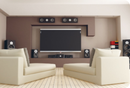 Fotografia de uma sala com decoração moderna. Uma televisão grande de tela fina, cercada de auto- falantes, em frente, duas poltronas com espaço para esticar as pernas.