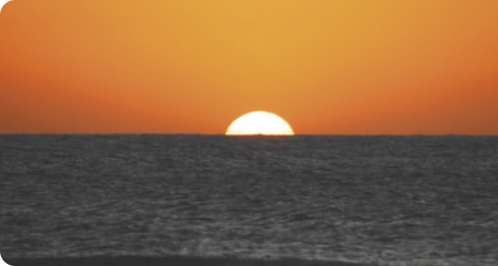 Fotografia de um pôr do Sol. O sol está refletindo sobre o mar.