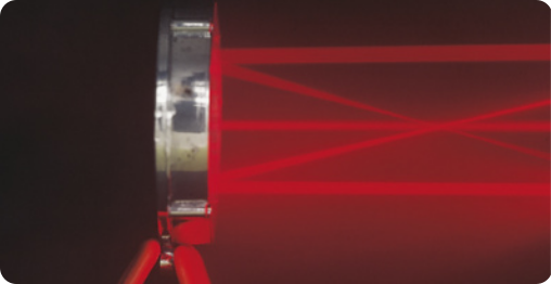 Imagem de um espelho côncavo, em formato redondo, com moldura de metal. Do espelho saem raios de luz vermelha horizontais, com um feixe central, outros dois feixes paralelos ao central, acima e abaixo, outros feixes cruzam a imagem geométrica formada pelos feixes.