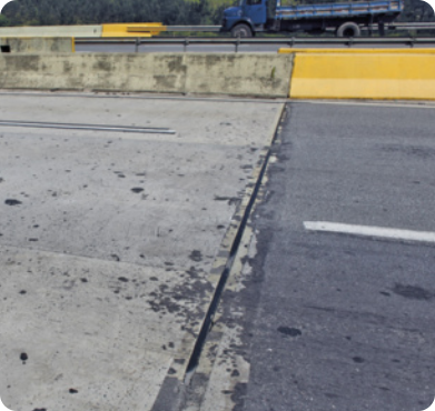 Fotografia da junta de dilatação em um trecho de estrada. Há um pequeno vão separando as duas placas de concreto.