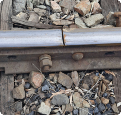 Fotografia de trilhos de trem. Eles são de metal e estão presos por parafusos. Há uma pequena fenda entre os trilhos.