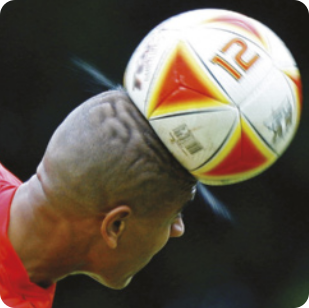 Fotografia de um jogador cabeceando uma bola. A bola está em cima da cabeça do jogador, seu formato redondo, está amassado com a cabeçada do jogador. O jogador está de costas. A bola tem desenhos triangulares estampados e o número 12.