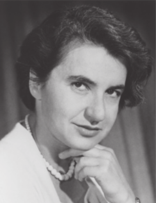 Fotografia em preto e branco de Rosalind Franklin posando com a mão embaixo do queixo. Ela é branca, tem cabelos curtos, pretos e lisos, e está usando paletó feminino e um colar.