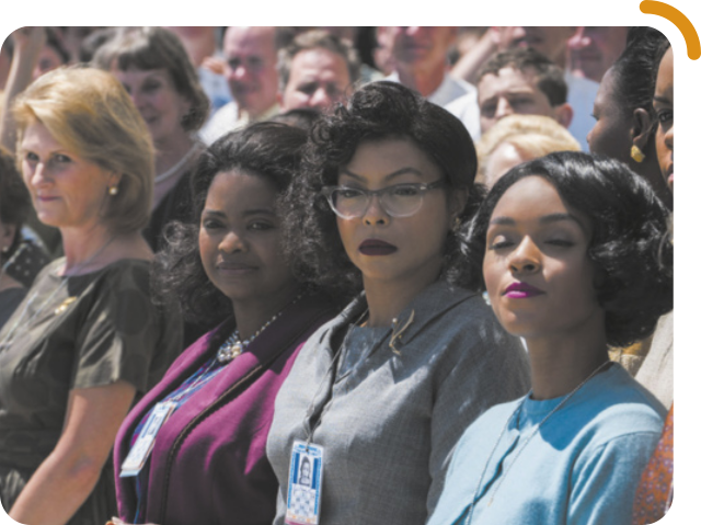 Cena do filme 'Hidden'. As três protagonistas do filme estão em pé, lado a lado, fazendo parte de um público. Elas estão observando atentamente algo à frente. São mulheres negras com cabelos com penteados, estão de maquiagem, roupas sociais de trabalho e usam crachá.