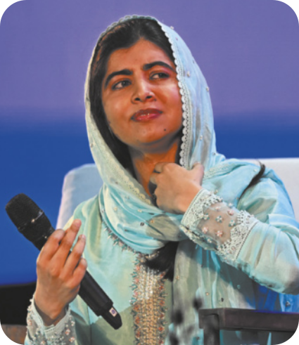 Fotografia de Malala Yousafzai. Ela tem pele clara e cabelos castanhos escuros, parcialmente cobertos por um véu em tons de azul. Está com expressão serena, um leve sorriso no rosto e olha para o lado, enquanto segura um microfone.
