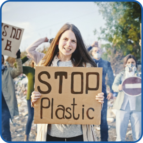 Fotografia de uma mulher segurando um cartaz com as duas mãos, onde está escrito 'STOP Plastic'. Ao fundo, outras pessoas também seguram cartazes e algumas levantam o braço com a mão fechada em sinal de protesto.