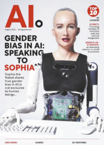 Capa da revista 'AI.' com as seguintes informações em destaque: 'Gender Bias in AI: Speaking to Sophia. Sophia the Robot shares how gender bias in AI is not exclusive to human beings...' A imagem que cobre a capa mostra a robô humanoide Sophia sentada à mesa, com uma das mãos sobre um teclado e a outra mão sobre um mouse de computador. Ela tem cobertura similar à pele humana no rosto e pescoço, de cor branca, com sobrancelhas castanhas e batom vermelho na boca. O topo da cabeça é transparente, mostrando os circuitos eletrônicos, assim como o ventre. Há uma câmera no meio do peito; o busto é preto e os braços, brancos e azuis.