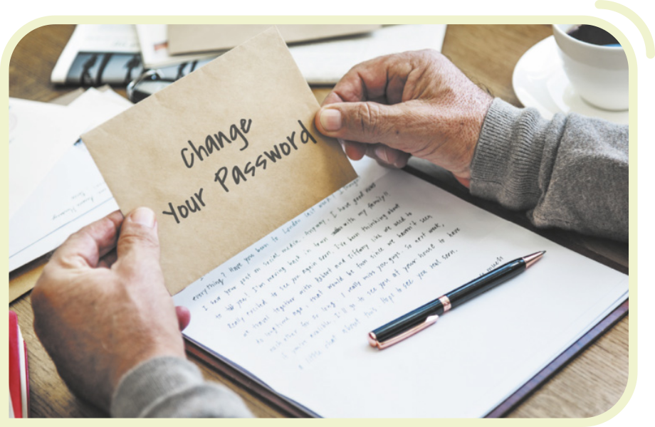 Fotografia das mãos de uma pessoa segurando um papel com a frase 'Change your password'. Abaixo, sobre uma mesa, há uma folha com um texto escrito em letra cursiva e uma caneta apoiada sobre ela.
