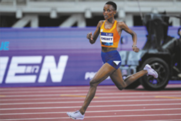 Fotografia de Beatrice Chebet correndo em uma pista de atletismo. Ela é negra, tem os cabelos raspados e está usando regata, shorts e tênis.