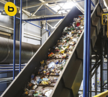 B. Fotografia de uma esteira em uma fábrica de reciclagem. Na esteira inclinada rolam resíduos.