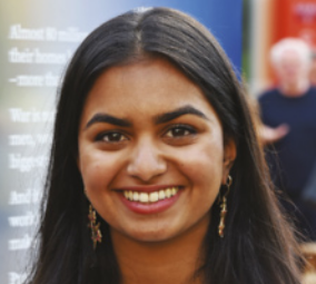 Fotografia de Amika George. Ela está sorrindo, tem cabelos longos e castanhos, soltos sobre os ombros.