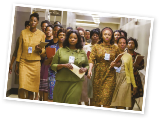 Cena do filme 'Hidden Figures'. Um grupo de mulheres caminha por um corredor, usando roupas formais. Algumas carregam pastas, cadernos ou documentos nas mãos. Elas estão em formação compacta, com expressão séria, e usam crachás de identificação.