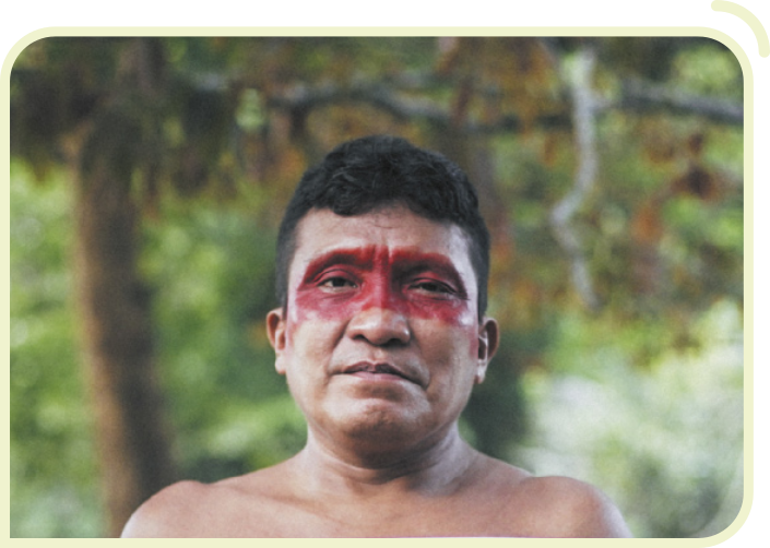 Fotografia de Joseca Yanomami. Ele é um homem indígena, usa o cabelo curto, pintura vermelha nos olhos e está sem camisa.