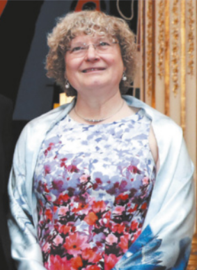 Fotografia de Ingrid Daubechies sorrindo. Ela é branca, tem cabelos curtos e ondulados e usa óculos, blusa estampada com flores e um xale, também estampado.