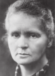 Fotografia em preto e branco de Marie Curie com expressão séria. Ela é branca, tem os cabelos grisalhos, presos para trás, e está usando uma blusa de gola estampada.