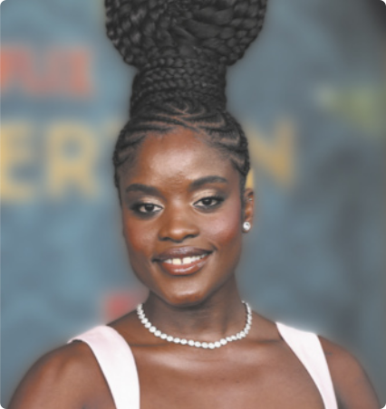 Fotografia de Ingrid Silva. Ela é uma mulher negra, com tranças nos cabelos, presas no topo da cabeça em um grande coque. Usa brincos, colar e está sorrindo.