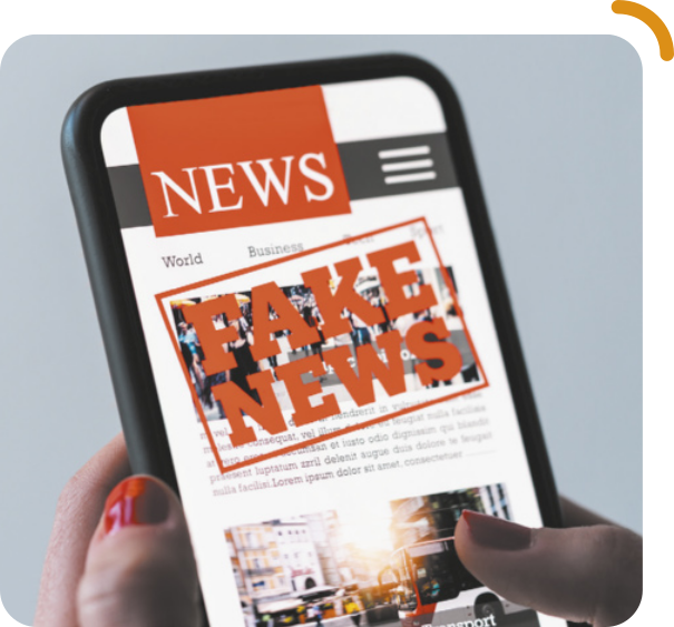 Fotografia de mãos segurando um celular. Na tela, no topo, aparece a palavra 'NEWS' e, sobre a imagem e o texto da matéria, está escrita a expressão 'FAKE NEWS', em vermelho, dentro de um retângulo.