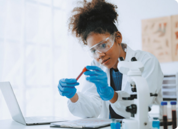Fotografia de uma mulher em um laboratório, manuseando um tubo de ensaio com líquido vermelho. Ela usa jaleco, luvas e óculos de proteção.
