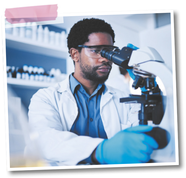 Fotografia de um homem regulando um microscópio em um laboratório. Ele usa jaleco, luvas e óculos de proteção.