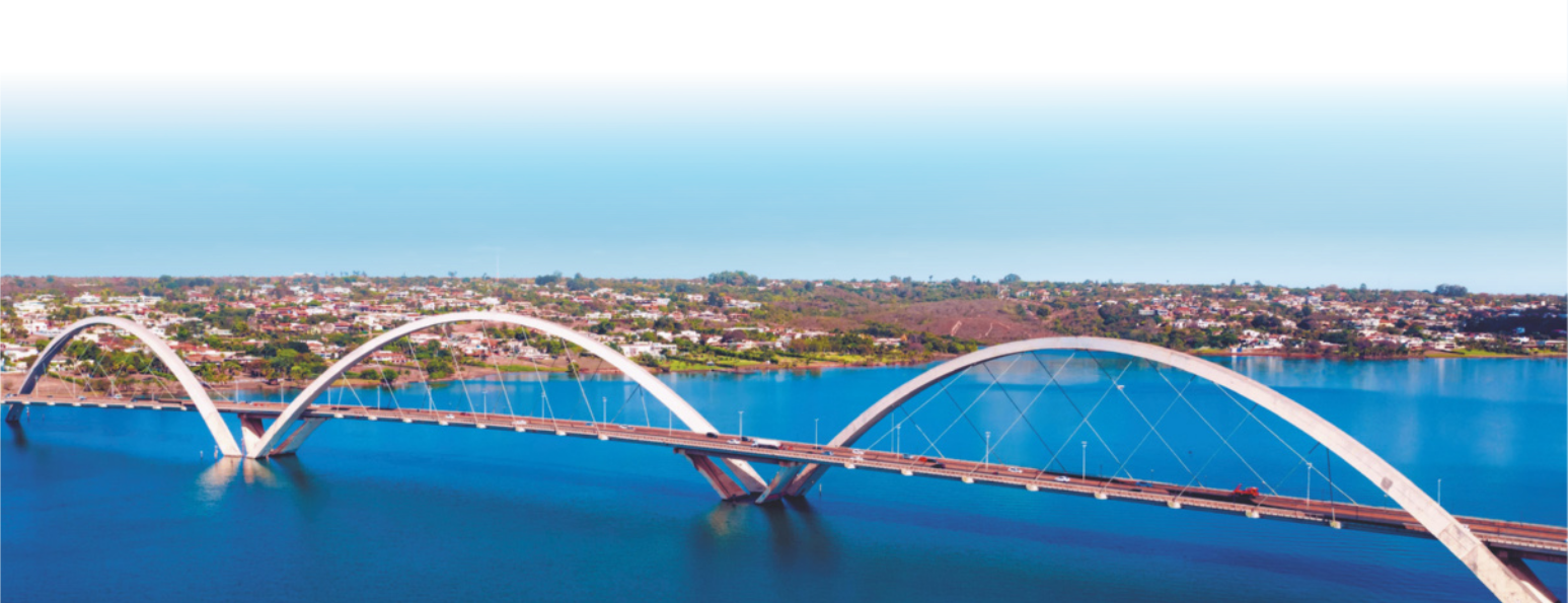 Fotografia de uma ponte retilínea atravessando um lago, sustentada por três grandes arcos que se assemelham a parábolas com concavidade voltada para baixo. Ao fundo, é possível observar áreas urbanas e vegetação.