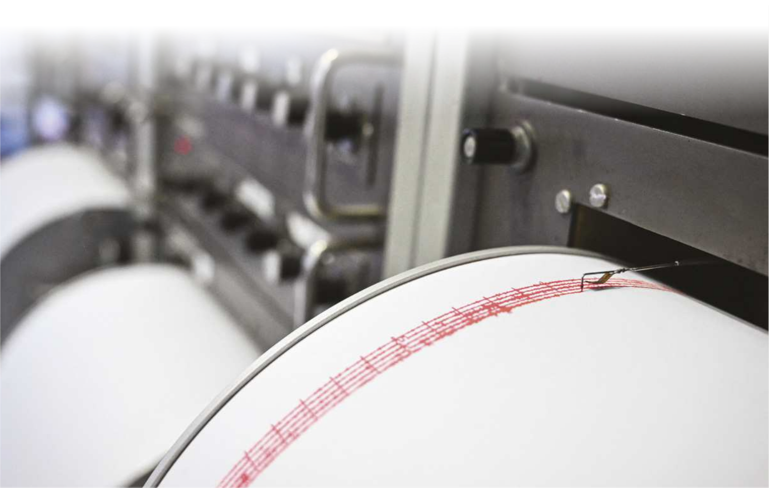 Fotografia de máquina com uma agulha com tinta que registra linhas em um papel. A maior parte das linhas está reta, mas há algumas oscilações concentradas.