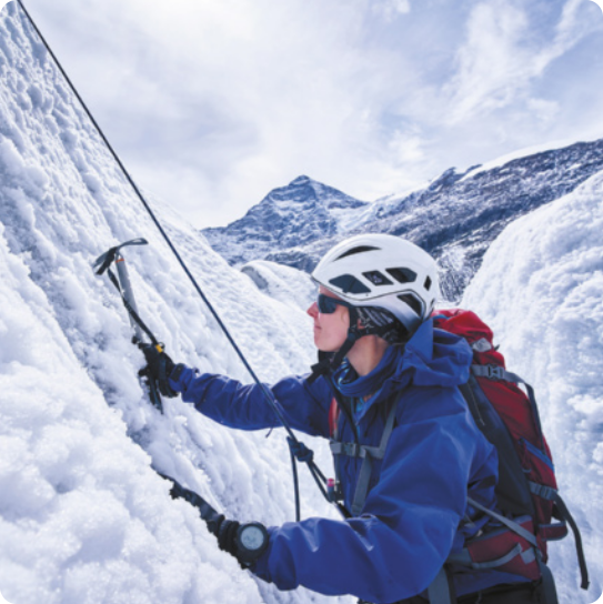 Imagem de alpinista utilizando uma ferramenta para subir uma montanha bastante íngreme, com neve.