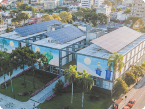 Fotografia com vista de cima de área urbana com grandes construções. Sobre o telhado delas, painéis de energia solar.