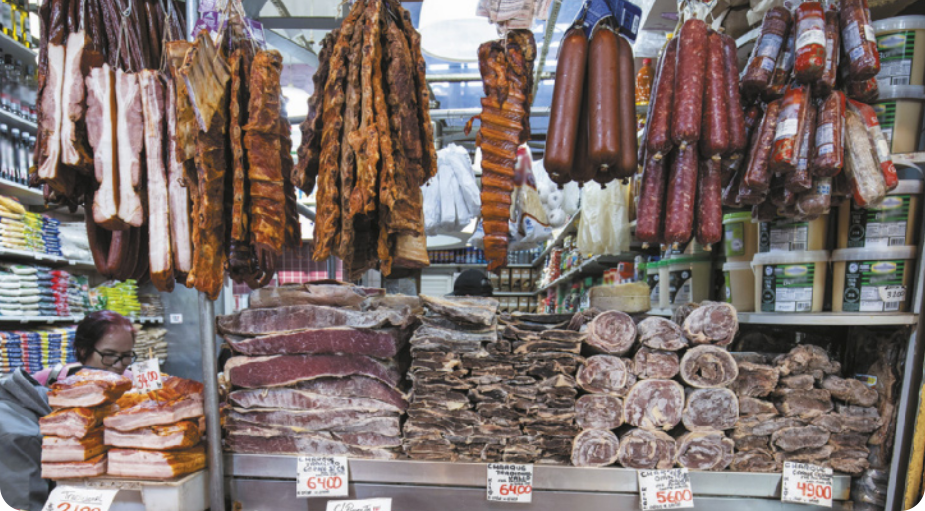 Fotografia de diversas carnes curadas sobre uma bancada e penduradas.