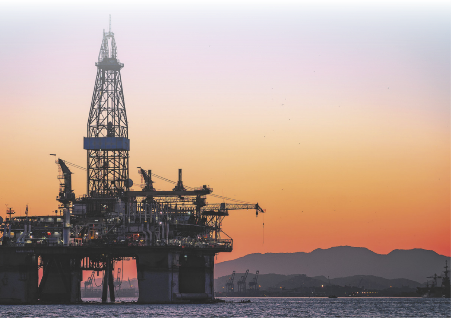 Fotografia de uma plataforma de petróleo no mar, durante o pôr do sol.