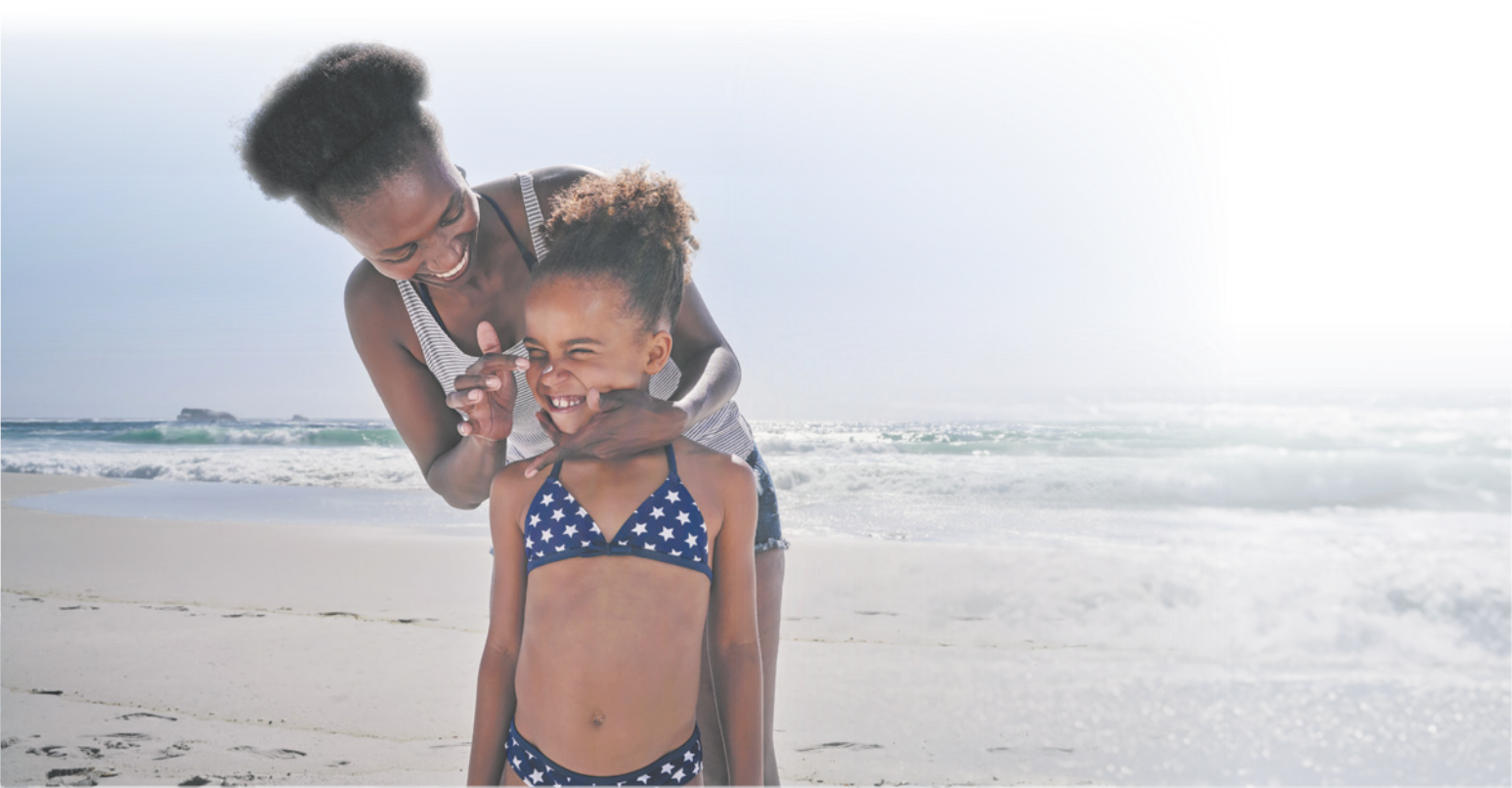 Fotografia de uma mulher passando protetor solar no rosto de uma menina, em uma praia.