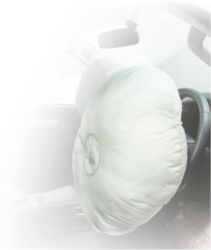 Fotografia de um airbag acionado. Ele é uma bolsa inflada arredondada fixada ao volante.